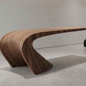 Op de afbeelding: Een lange, horizontale tafel opgebouwd uit gelaagd, donkerbruin hout. De structuur heeft een doorlopende, vloeiende curve die overgaat van een brede, geribbelde basis naar een plat, uitgestrekt oppervlak, wat een zwevend effect creëert met een gladde afwerking.