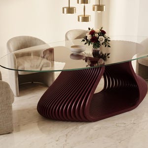 May include: An oval glass dining table with a dark burgundy, slatted, sculptural base. The table is surrounded by four beige upholstered barrel chairs. A small bowl and a bouquet of red and white flowers sit on the glass surface.