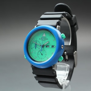 May include: A Seiko Rugby Timer Quartz watch featuring a blue bezel and a green dial. The watch has a black rubber strap and green buttons. The watch face displays the time and date.