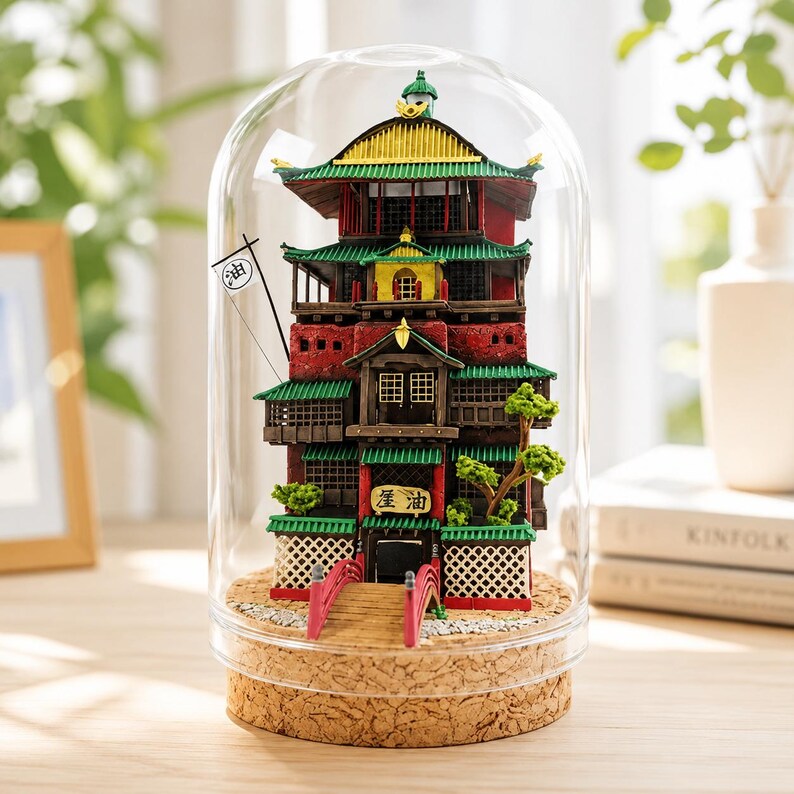 K&ouml;nnte beinhalten: Ein Miniaturmodell eines mehrst&ouml;ckigen Geb&auml;udes im japanischen Stil, eingeschlossen in einer klaren Glaskuppel mit Korkboden. Das Bauwerk hat rote W&auml;nde, gr&uuml;ne Ziegeld&auml;cher, eine kleine rote Bogenbr&uuml;cke und eine wei&szlig;e Flagge mit dem Kanji-Zeichen 油.
