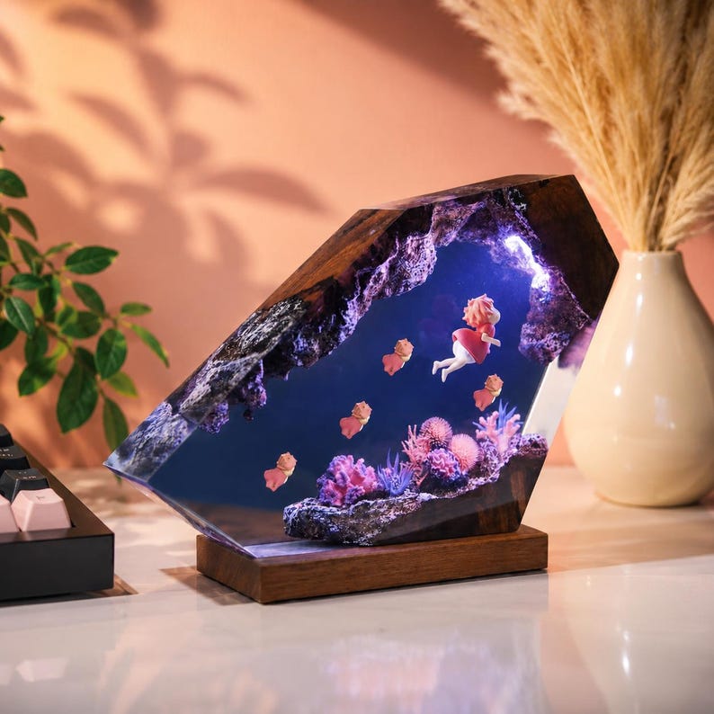 May include: A rectangular resin lamp featuring a dark wood base and a polished wood frame. Inside the clear resin, a miniature scene depicts a small figure in a red dress swimming among pink and purple coral formations and several small fish.