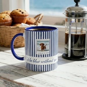 Puede incluir: Una taza de cerámica con un patrón de rayas verticales azules y blancas. La taza presenta una foto cuadrada de un perro salchicha marrón en una playa con el texto 'Greta at the beach' y la frase 'I'd be blue without you' en azul.