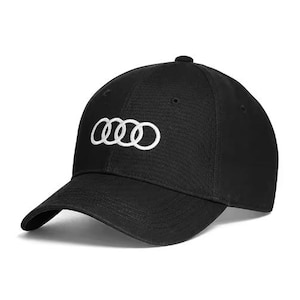 May include: Black baseball cap featuring the Audi logo in white. The cap has a curved brim and a button on top. The Audi logo consists of four interlocking rings.