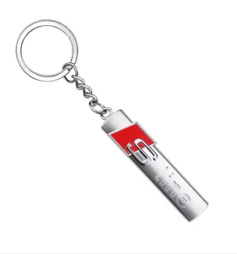 May include: Silver-coloured keyring with a rectangular pendant featuring a red accent and the letters "S" and "line" in a stylized font. The keyring includes a ring and a chain.