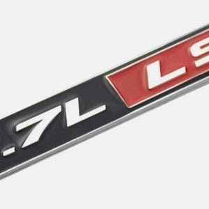 Op de afbeelding: Een rechthoekig embleem met de tekst "5.7L LS1" in witte letters. Het embleem heeft een zwarte basis met een rode rechthoek aan het einde. Het embleem is waarschijnlijk voor een voertuig.