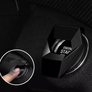May include: Black car engine start button with a faceted design. The button has the words "ENGINE START" printed on it. The button is shown installed in a car's interior.