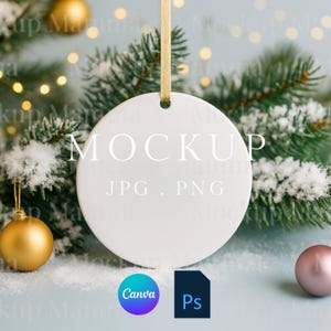 以下が含まれることがあります： 中央に「MOCKUP」の文字が入った、白い丸いクリスマスオーナメントのモックアップ。オーナメントは金色のリボンで吊り下げられており、背景には雪の積もった常緑樹の枝があります。「JPG . PNG」の文字は「MOCKUP」の下にあります。