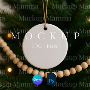 以下が含まれることがあります： 白い丸いセラミックオーナメントで、白い文字で「MOCKUP」と書かれています。オーナメントは、クリスマスツリーと木製のビーズのぼやけた背景に対して、金の紐で吊り下げられています。CanvaとPhotoshopのロゴが含まれています。