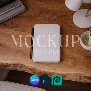 Puede incluir: Un cuaderno blanco encuadernado en cuero con un bolígrafo negro, sobre una superficie de madera. La palabra "MOCKUP" se muestra en letras grandes y claras. Debajo, las palabras "PSD + PNG". Los iconos de Canva, Ps y P son visibles.