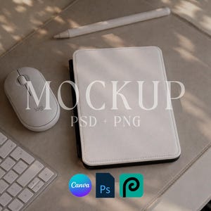 Puede incluir: Una funda blanca para tableta, un ratón y un lápiz óptico están colocados sobre una superficie de tonos neutros. La palabra "MOCKUP" se muestra en letras grandes y claras. El texto "PSD + PNG" está debajo.