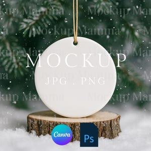 以下が含まれることがあります： 「MOCKUP」の文字がプリントされた白い丸いセラミックオーナメント。金色の紐で吊るされており、木の輪切りに飾られています。雪の背景と常緑樹の枝が背景にあります。CanvaとPsのロゴが見えます。