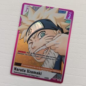 May include: A rectangular Naruto Uzumaki trading card with a metallic pink border. The card features a blonde character with a blue headband, gold background, and text including Activate Main, power 3, and life 15. The card is labeled Naruto Uzumaki.