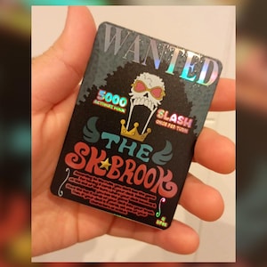 Puede incluir: Una tarjeta negra e iridiscente con el texto "WANTED" en la parte superior. La tarjeta presenta una calavera con gafas de sol, una corona y las palabras "THE SKBROOK". La tarjeta también incluye el texto "5000 ACTIVATE MAIN" y "SLASH ONCE PER TURN".