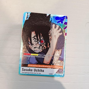 May include: A rectangular trading card featuring an illustration of Sasuke Uchiha with black hair and red eyes. The card has a holographic finish, blue borders, and text including "Sasuke Uchiha," "Fire/Lightning/Uchiha Clan/The Taka," and "LIFE 15."