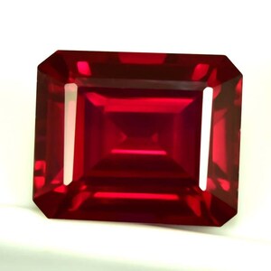 Peut inclure: Une pierre précieuse rubis de coupe rectangulaire vibrante. La gemme est d'un rouge profond et riche avec une surface à facettes qui reflète la lumière. La coupe est de forme émeraude, avec un corps rectangulaire et des coins biseautés. La pierre est sur fond blanc.