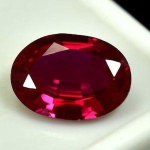 Op de afbeelding: Een gefacetteerde, ovaalvormige robijn edelsteen. De edelsteen heeft een diepe, verzadigde rode kleur met heldere, reflecterende facetten. De robijn is geplaatst tegen een witte achtergrond, wat de kleur en helderheid benadrukt. Geschikt voor sieraden.