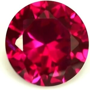 May include: A round, faceted ruby gemstone. The gem is a deep, vibrant red color with multiple facets that reflect light. The gemstone is set against a white background.