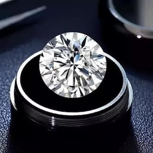 Könnte beinhalten: Ein brillantgeschliffener Diamant, gefasst in einem schwarz-silbernen Ring. Der Diamant funkelt mit vielen Facetten und reflektiert das Licht. Der Ring hat ein schlankes, modernes Design mit schwarzem Innenraum und silbernem Band. Nahaufnahme.