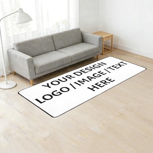 May include: A rectangular white rug with a black border, featuring the text "YOUR DESIGN LOGO / IMAGE / TEXT HERE" in bold black letters. The rug is placed on a light-colored wooden floor, with a gray sofa and a side table in the background.