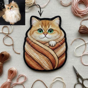 Op de afbeelding: Geborduurde patch met een gouden kat met heldergroene ogen, gewikkeld in een gestreepte deken. De patch heeft een zwarte rand en is omgeven door klosjes garen en een foto van de kat. Een charmant item met katten als thema.