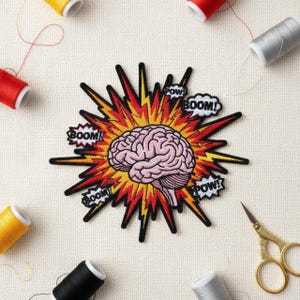 May include: Embroidered patch featuring a pink brain at the center of a red and yellow explosion design. The patch includes speech bubbles with the words "BOOM!" and "POW!" in black. Sewing supplies surround the patch.