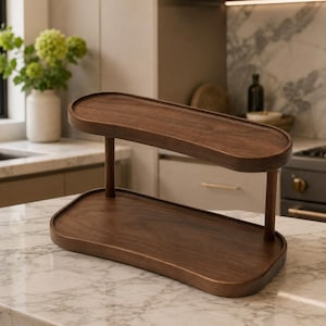 May include: A two-tiered display stand crafted from dark brown wood, featuring two smooth, oval-shaped trays connected by two vertical cylindrical supports. The structure has a polished finish, showcasing the natural wood grain throughout the surface.