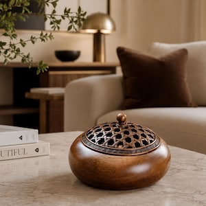 May include: A round, polished dark wood incense burner featuring a removable metal lid with a woven lattice pattern and a Greek key border design. The burner has a smooth, curved base and a small spherical knob at the center of the lid.