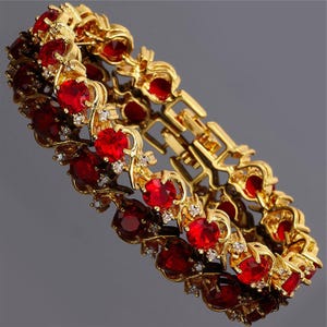 Può includere: Bracciale dorato con una serie di vivaci pietre preziose rosse, intervallate da piccoli accenti scintillanti. Il design del bracciale incorpora dettagli intricati, creando un gioiello lussuoso e accattivante.