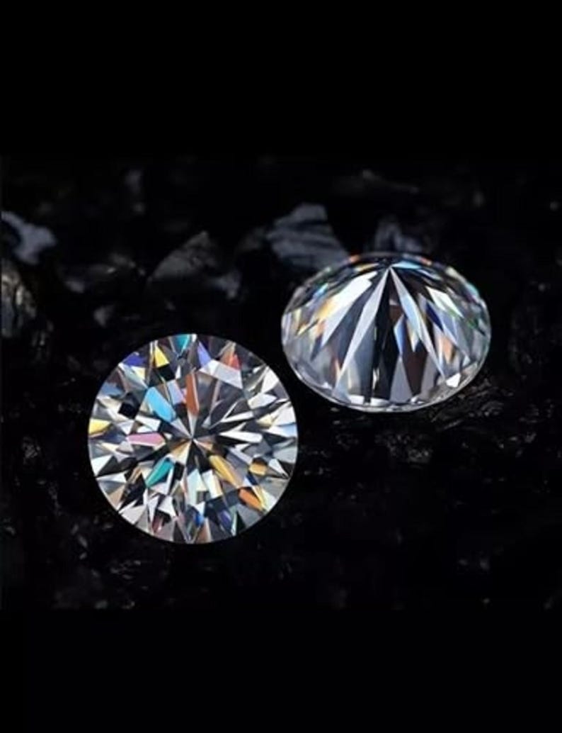 Puede incluir: Dos gemas redondas y claras, con intrincadas facetas, se muestran sobre un fondo oscuro. Las gemas brillan, reflejando varios colores de luz. Las gemas son probablemente diamantes o simulaciones de diamantes.