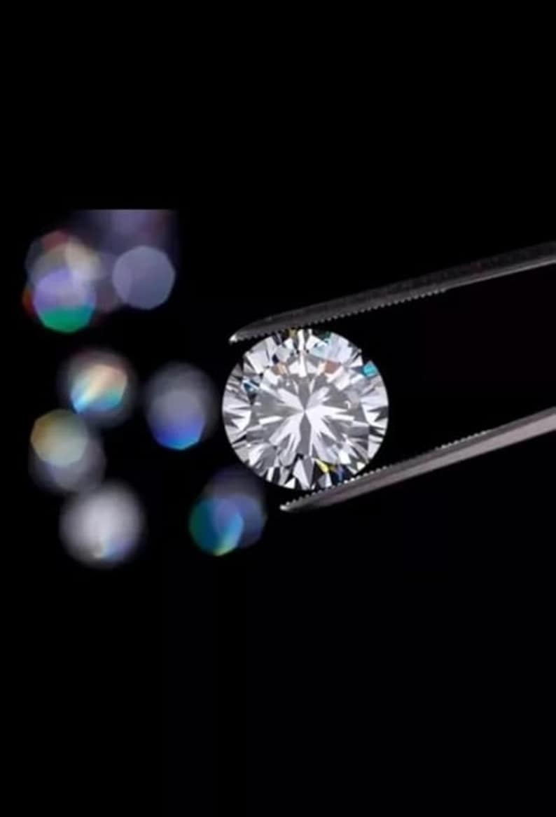 Puede incluir: Un diamante de talla brillante, sostenido por unas pinzas sobre un fondo negro. Las facetas del diamante reflejan la luz, creando un efecto brillante. El fondo est&aacute; borroso, con bokeh, atrayendo la atenci&oacute;n hacia la gema.