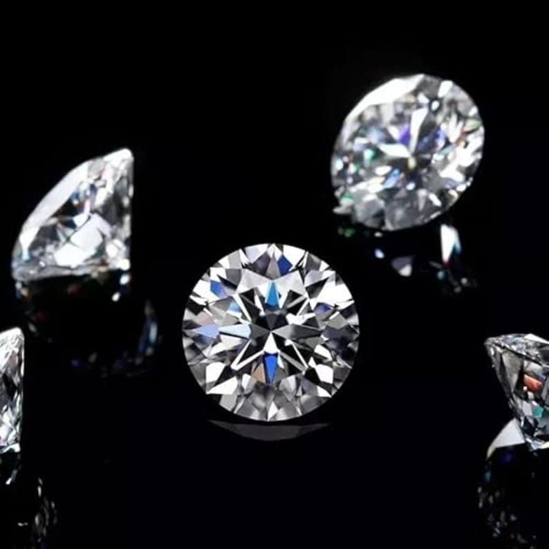 Puede incluir: Varios diamantes de talla brillante se muestran sobre un fondo negro. Los diamantes, claros y facetados, reflejan la luz creando un efecto brillante. La imagen destaca la claridad y el brillo de las piedras preciosas.