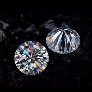 Puede incluir: Dos gemas redondas y claras, con intrincadas facetas, se muestran sobre un fondo oscuro. Las gemas brillan, reflejando varios colores de luz. Las gemas son probablemente diamantes o simulaciones de diamantes.