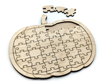 Op de afbeelding: Een houten pompoenvormige legpuzzel met enkele ontbrekende stukjes. De puzzel is gemaakt van lichtgekleurd hout met donkere contouren. Verschillende puzzelstukjes liggen verspreid rond de pompoenvorm.