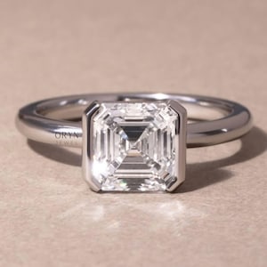 May include: A close-up of a silver ring with a large, square-cut, clear gemstone. The ring has a smooth, rounded band and the gemstone is set in a bezel setting. The brand name "ORYN JEWEL" is visible on the ring.
