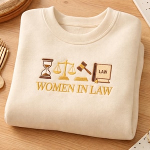 Könnte beinhalten: Ein Set aus drei Keramikbechern mit gesprenkelter, cremefarbener Glasur. Jeder Becher zeigt ein handgemaltes Design: ein blaues und grünes Blatt, eine gelbe Blume und eine rote Beere. Die Becher haben eine einfache, abgerundete Form.