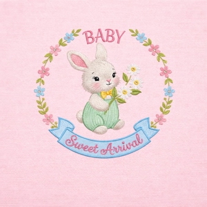 Puede incluir: Diseño bordado con un conejito blanco con pajarita amarilla y peto verde, sosteniendo margaritas. El diseño incluye la palabra "BABY" arriba y "Sweet Arrival" en una pancarta azul, rodeado de una corona floral sobre fondo rosa.