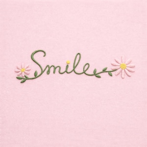 Puede incluir: Tela rosa con bordado verde de la palabra "Smile". Dos flores de margarita, con centros amarillos y pétalos rosas, enmarcan el texto. El bordado tiene un aspecto delicado y artesanal.