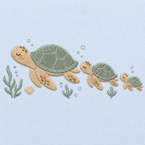 May include: An embroidery design on a light blue background featuring three sea turtles of decreasing size swimming from left to right. The turtles have tan bodies, sage green shells, and closed eyes. Small green seaweed sprigs, a shell, and bubbles surround them.