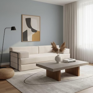 May include: A contemporary living room featuring a cream sofa, a grey coffee table with wooden supports, and a framed abstract artwork. The room has a light blue wall, a black floor lamp, and a woven footstool. The sofa is approximately 200 cm long.