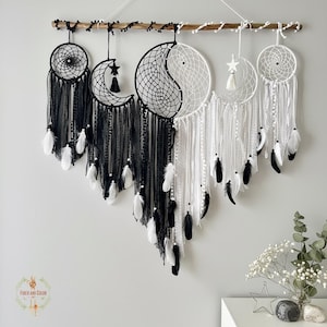 May include: A collection of handmade dream catchers in black and white, hanging from a wooden branch. The dream catchers feature intricate web designs, feathers, and moon and star accents. The overall design is a blend of bohemian and celestial themes.