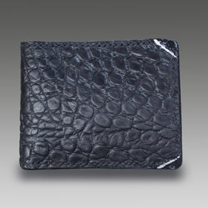 May include: A dark blue, bi-fold wallet with a textured, crocodile-like pattern. The wallet has a stitched border and white accents on the corners. The wallet is made of a durable material.
