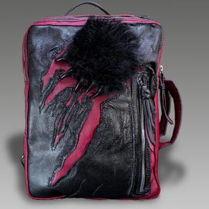 Può includere: Zaino in pelle nera e rossa con design ad artiglio. Lo zaino presenta un accento di pelliccia nera e una tasca con cerniera. La borsa ha un manico superiore e una tracolla. Le dimensioni sono di circa 30 cm di larghezza, 38 cm di altezza e 10 cm di profondità.