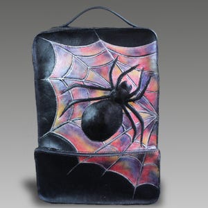 Può includere: Uno zaino in pelle nera con un design inciso e dipinto a mano raffigurante un grande ragno nero al centro di una vivace ragnatela multicolore. La borsa include una maniglia superiore, una tasca frontale con cerniera e una chiusura a zip.