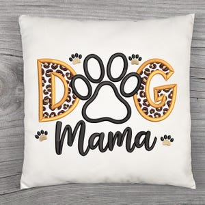 May include: White square pillow with the words "Dog Mama" in black script. The letters "D" and "G" have a leopard print design with gold trim. A black paw print is in the center, with smaller paw prints around the text.