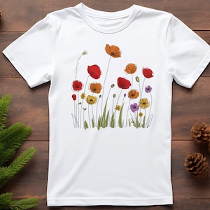 May include: White t-shirt featuring a colorful floral design. The graphic includes red, orange, yellow, and purple flowers with green stems and leaves. The flowers are stylized with black outlines, creating a whimsical and artistic look.