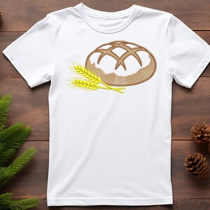 Peut inclure: T-shirt blanc avec un motif brod&eacute; d'un pain avec un dessus quadrill&eacute; et deux &eacute;pis de bl&eacute;. Le pain est marron et blanc, et le bl&eacute; est jaune et vert.