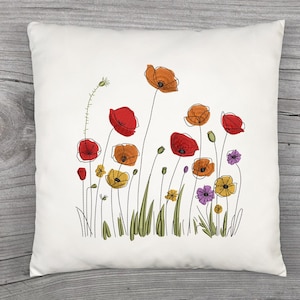May include: A square, white throw pillow featuring an embroidered floral design. The design includes red, orange, yellow, and purple poppies with green stems and leaves. The pillow is placed on a wooden surface.