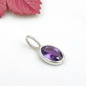 Op de afbeelding: Een zilveren hanger met een ovale, dieppaarse edelsteen. De hanger heeft een eenvoudig, elegant ontwerp met een lus aan de bovenkant voor een ketting. De edelsteen is gezet in een zilveren bezel, wat een klassieke uitstraling geeft.