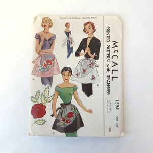 May include: Vintage McCall's printed sewing pattern for women's organdy aprons. The cover features illustrations of aprons with floral designs. The pattern includes the text "PRINTED PATTERN with TRANSFER" and the number "1594".