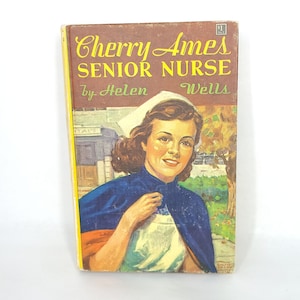 May include: A vintage paperback book cover featuring a young woman in a nurse's uniform. The book title is "Cherry Ames Senior Nurse" by Helen Wells.